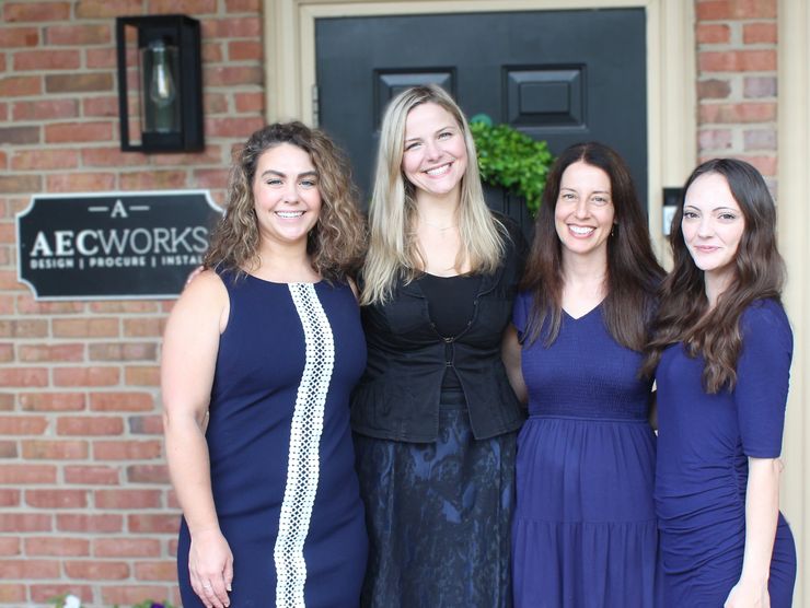 Four women smiling in front of an AECWORKS sign.